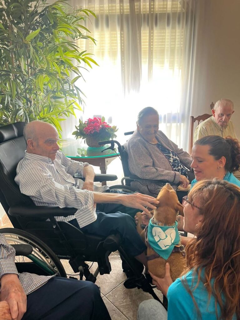 Residente sonriendo mientras otro acaricia a un perro pequeño de terapia